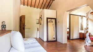 Una habitación amplia con techo de madera, sofá blanco, cama con ropa de cama blanca y suelo de madera.