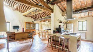 Una cocina rústica con vigas de madera a la vista, una pared de piedra y una zona de comedor de madera con un banco.