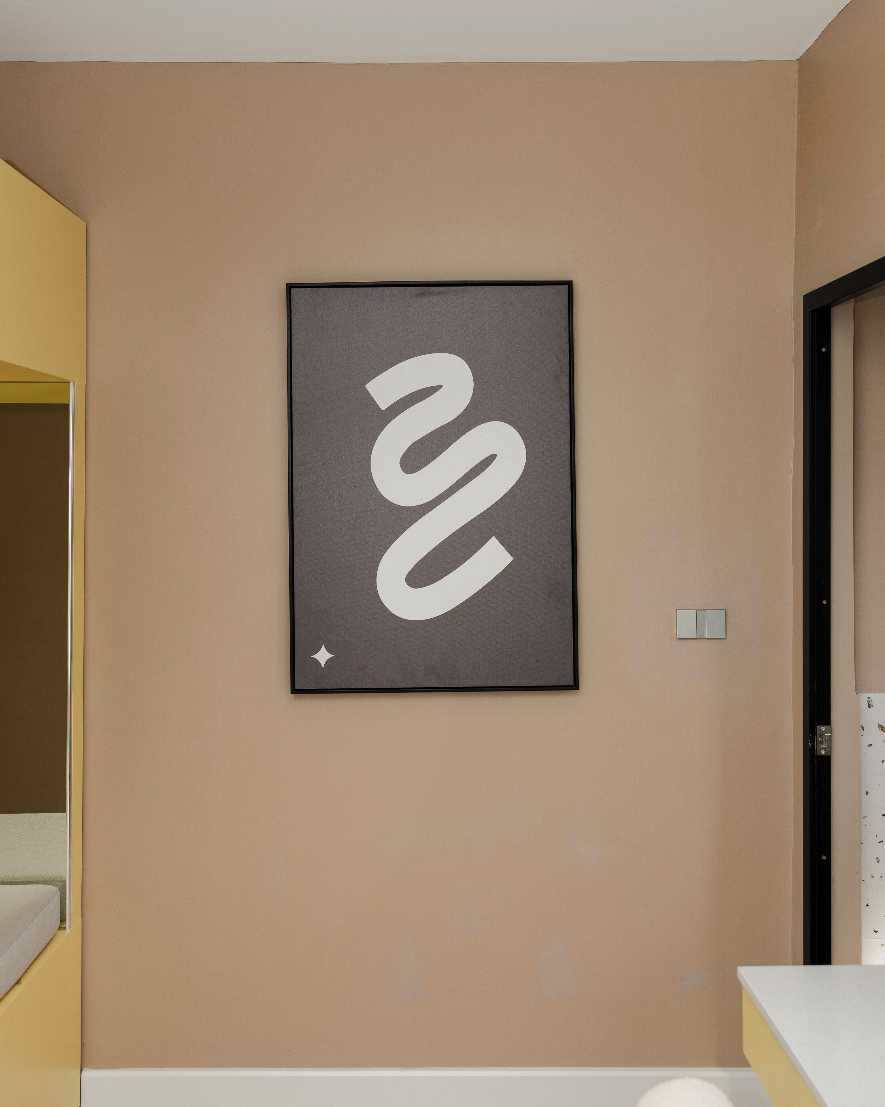Una obra de arte abstracta en marco sobre una pared color beige en una habitación de hotel.