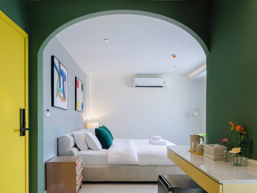 Una habitación de hotel moderna con cama, escritorio y kitchenette. Hay obras de arte enmarcadas en la pared y un equipo de aire acondicionado montado allí.