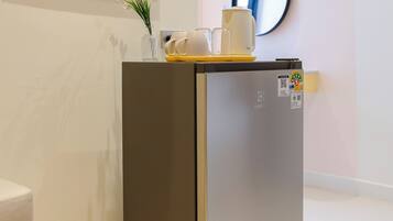 A compact, modern refrigerator in a clean, minimalistic room with a framed artwork on the wall and a small vase with flowers on top.