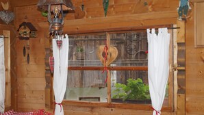 A wooden cabin interior with a bed, checkered pillows, a window with heart-shaped decorations, and a hanging lantern. - Traditional Apartment "Waldstille" in Idyllic Nature, Balcony and Wi-Fi (San Lorenzo di Sebato)