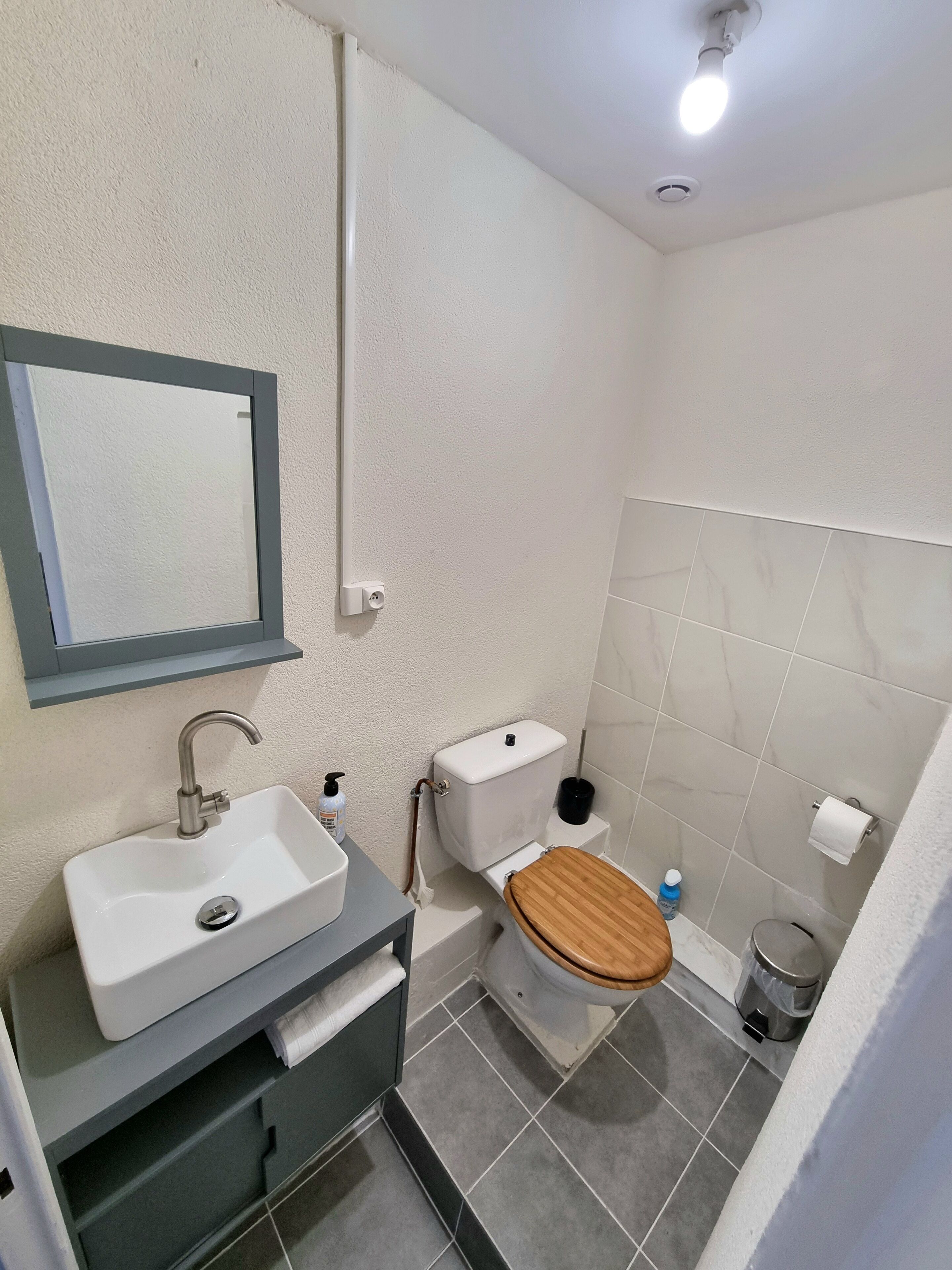 A small, clean bathroom with a white sink, mirror, toilet, and shower.