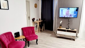 Una sala de estar moderna con una televisión, dos sillones rojos, un sofá gris y una pequeña mesa de madera.
