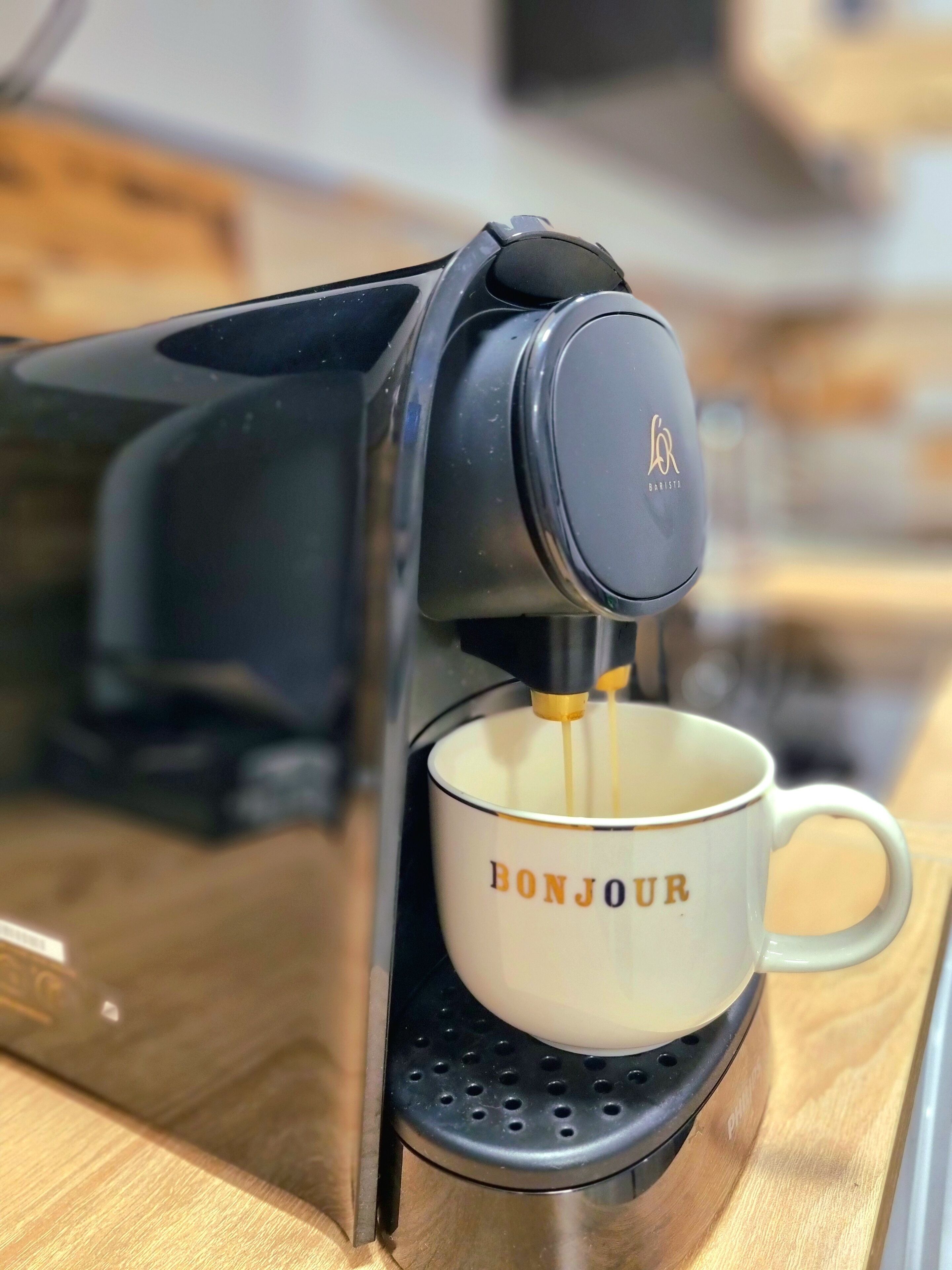 A coffee machine dispensing coffee into a mug with "BONJOUR" written on it.