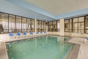 Una piscina interior con paredes de vidrio transparente, sillas azules y un ventilador.