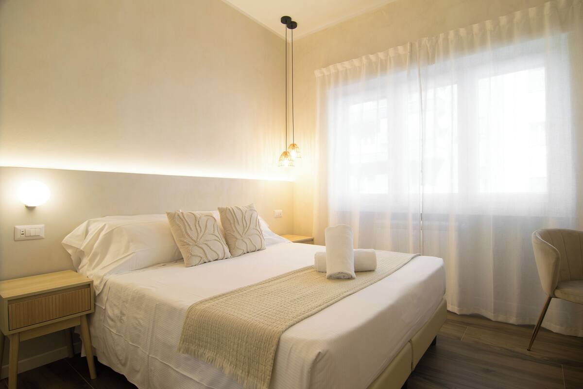A neatly made bed with a blanket, pillows, and a bedside lamp.