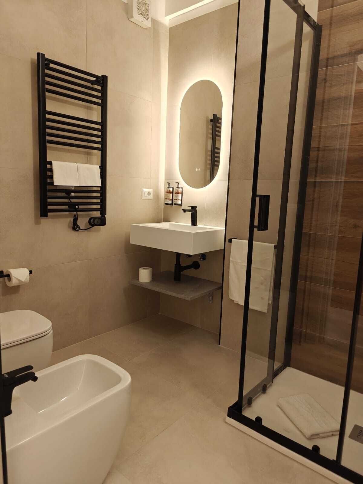 Un baño moderno con ducha de vidrio, bañera blanca, lavamanos con espejo y toallero.