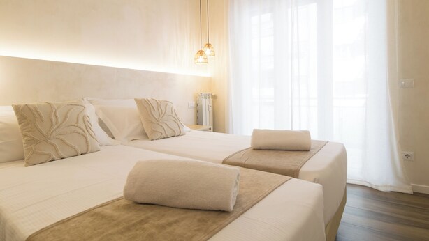 A hotel room with two beds, a large window with sheer curtains, and a hanging light fixture. - Lilla Eco House Vaticano (Rome)
