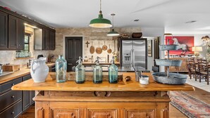 A kitchen with a wooden island, hanging pots, and a zebra painting. - Pool, Porch & Stunning Views: Spacious Texas Home! (Glen Rose)