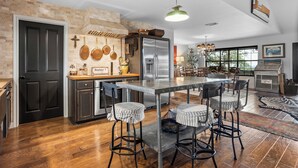 A spacious kitchen with a central island, dark cabinetry, and a rustic brick wall. - Pool, Porch & Stunning Views: Spacious Texas Home! (Glen Rose)