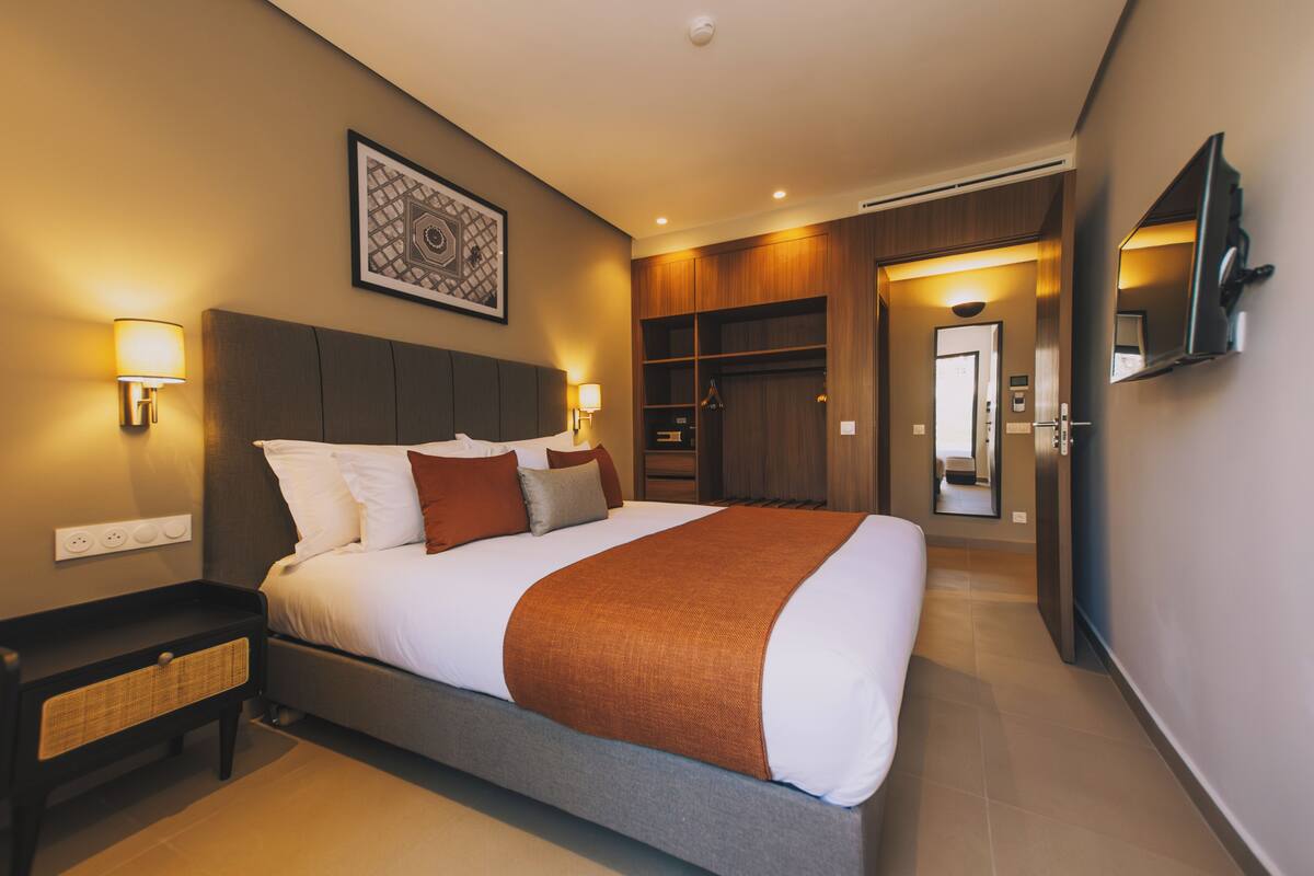 A modern hotel room with a large bed, bedside lamps, a wardrobe, and a television mounted on the wall.