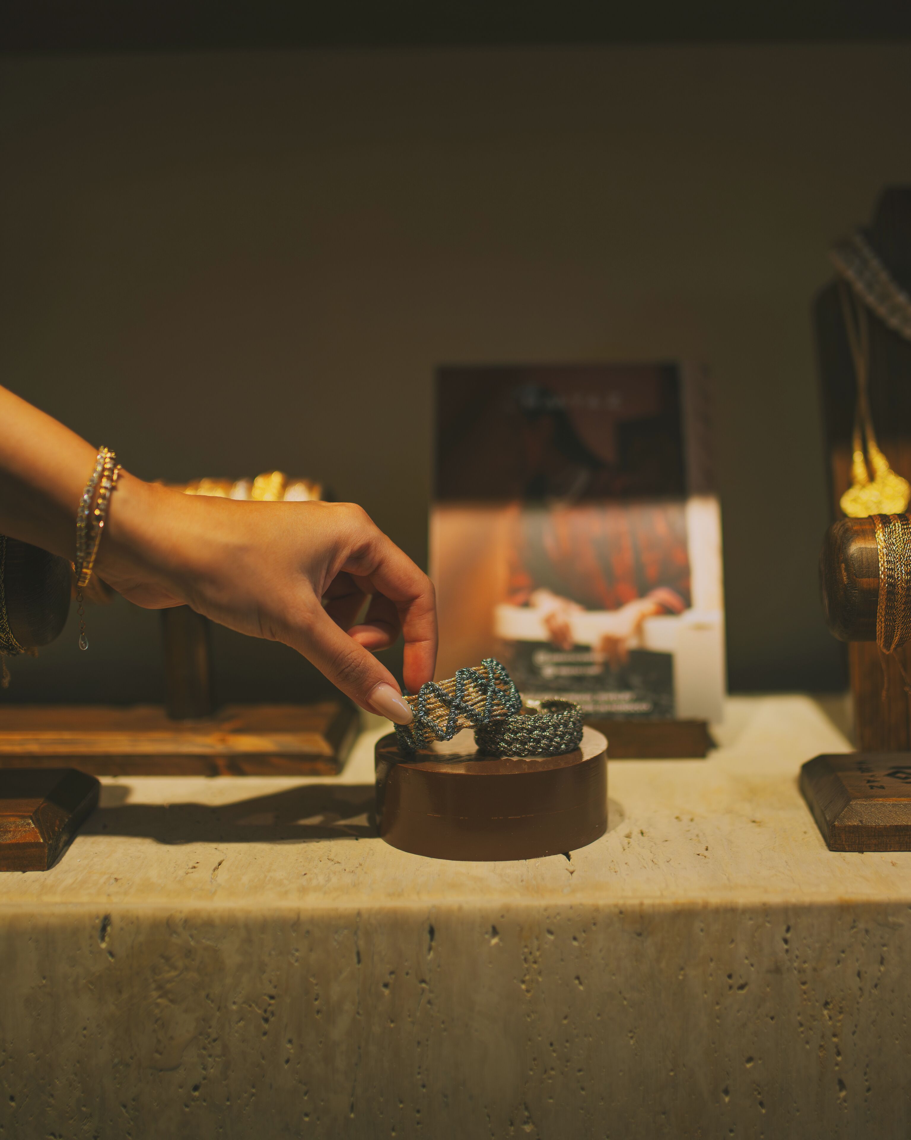 A hand holding a small, intricately woven object, possibly a piece of jewelry, on a wooden surface with a blurred background.