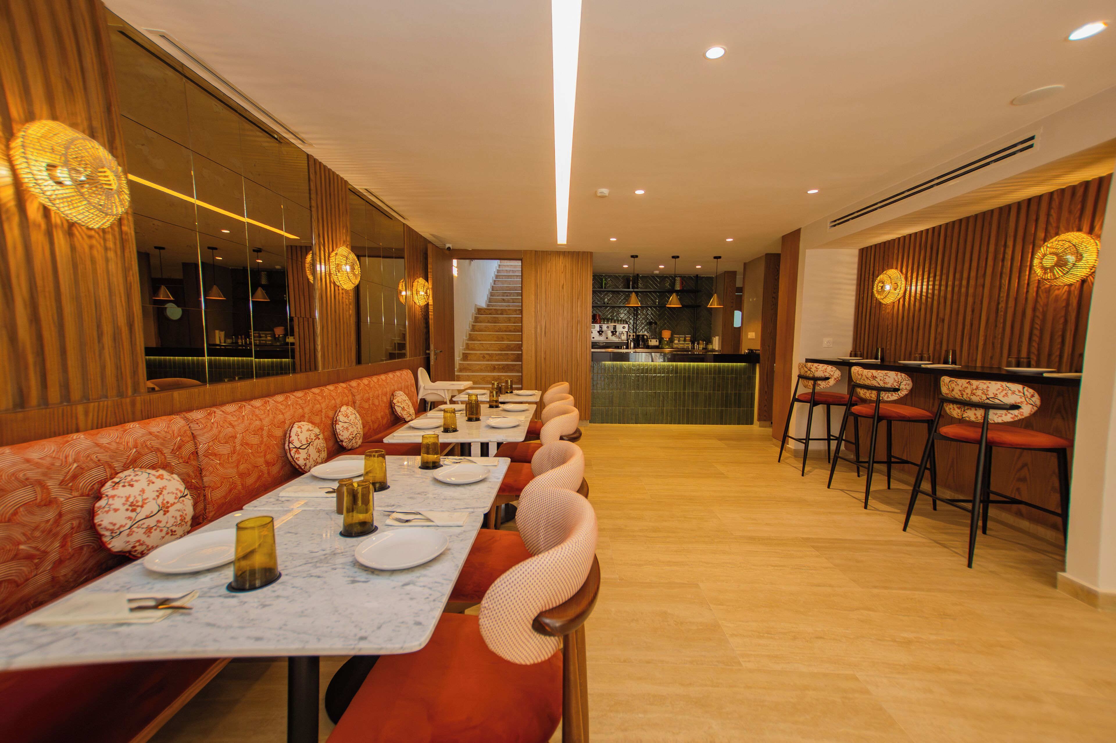 A restaurant with a long dining table, cushioned booths, and a bar area.