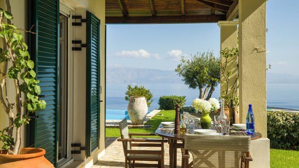 An outdoor patio with a table set for dining, overlooking a scenic view of the sea and mountains. - Villa Pelagos & guest house, undoubtedly has one of the best views in Corfu. (Corfu)