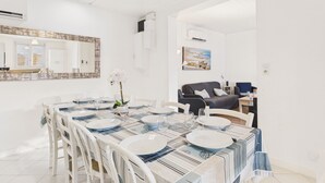 Een eetruimte met een lange tafel voor vier personen, witte stoelen en een moderne hanglamp.