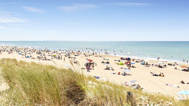 Een druk strand met mensen die zonnebaden en langs de kust wandelen.