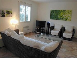 A living room with a wicker sofa, a glass coffee table, a TV, and a painting on the wall. - Magnificent villa with private pool in a quiet location (vidauban)