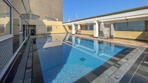 En pool på taket med kristallklart blått vatten, omgiven av modern arkitektur och en klar himmel.