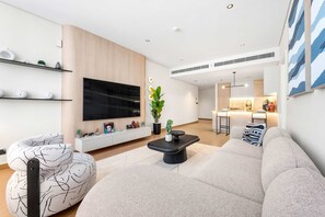 Ein modernes Wohnzimmer mit Sofa, Couchtisch, Fernseher und einer Küche im Hintergrund.