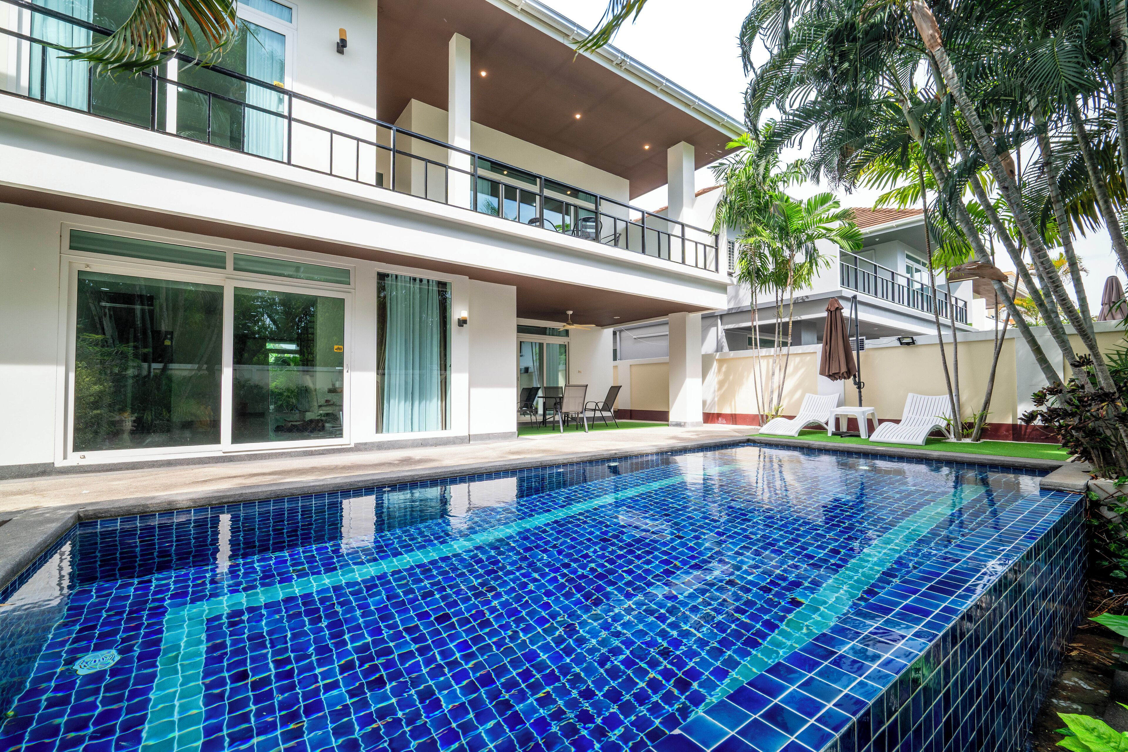 A modern two-story house with a swimming pool, large windows, and a balcony.