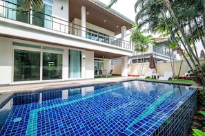 Uma casa moderna de dois andares com piscina, grandes janelas e uma varanda.