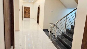 Un pasillo moderno de hotel con piso de mármol, una escalera con barandillas de metal e iluminación empotrada.