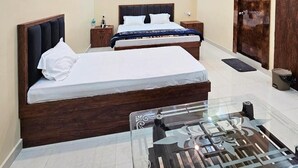Habitación de hotel con dos camas, una mesa de centro de vidrio, un armario de madera y una mesita de noche con una lámpara.