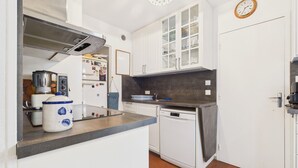 Une cuisine compacte avec des meubles blancs, un lave-vaisselle, une machine à café et une bouilloire.
