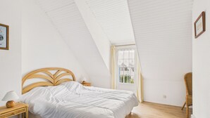 Une chambre avec un plafond en pente, un lit, une table de chevet, une chaise et une fenêtre.