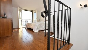 Ein Schlafzimmer mit Holzboden, einem Bett mit weißer Bettdecke, einer Balkontür und einer Treppe mit schwarzer Geländer.