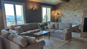 A living room with a stone fireplace, large windows, and a view of the outdoors. - Maison Belle Vue  – Charming villa with pool & breathtaking views - Near Nice (Carros)