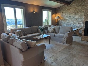 A living room with a stone fireplace, large windows, and a view of the outdoors. - Maison Belle Vue  – Charming villa with pool & breathtaking views - Near Nice (Carros)