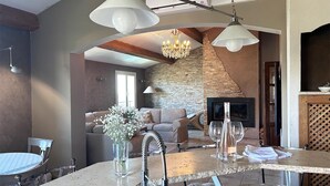 A modern living room with a stone fireplace, a chandelier, and a dining area with a marble table. - Maison Belle Vue  – Charming villa with pool & breathtaking views - Near Nice (Carros)