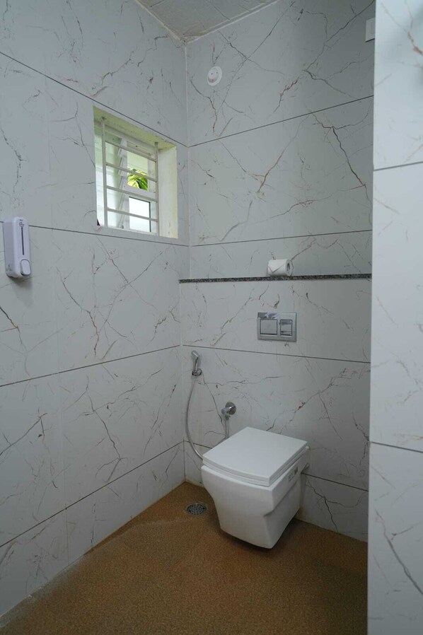 Un baño pequeño con paredes de mármol blanco, un inodoro blanco, una ducha y una ventana con una planta.