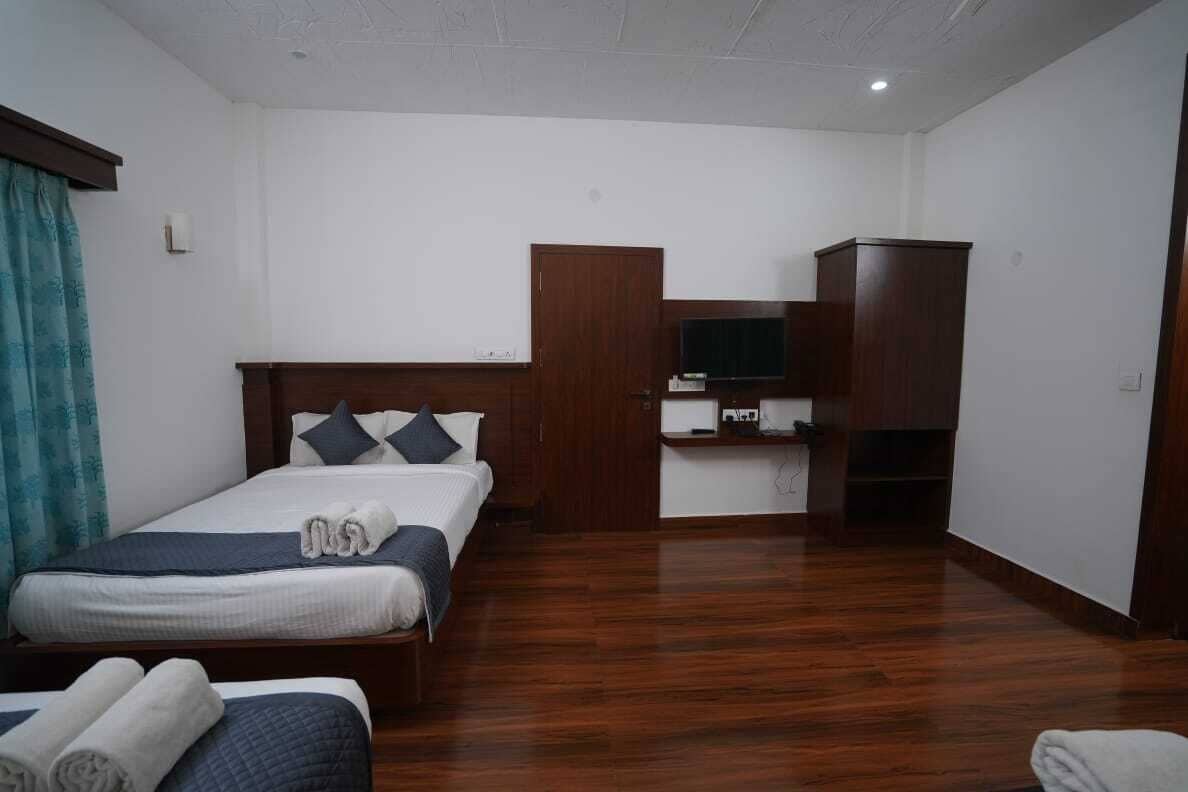 A hotel room with a wooden floor, a bed with a headboard, a TV mounted on the wall, and a wooden wardrobe.