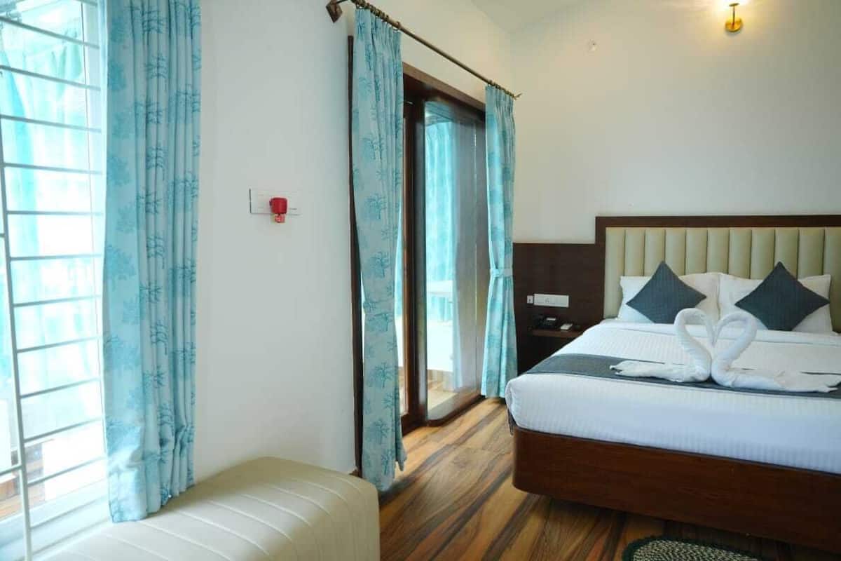 Een hotelkamer met een bed, een bankje, een nachtkastje en een deur naar een balkon.