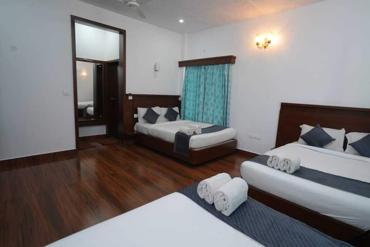 Een hotelkamer met twee bedden, houten vloeren, een spiegel en een raam met gordijnen.