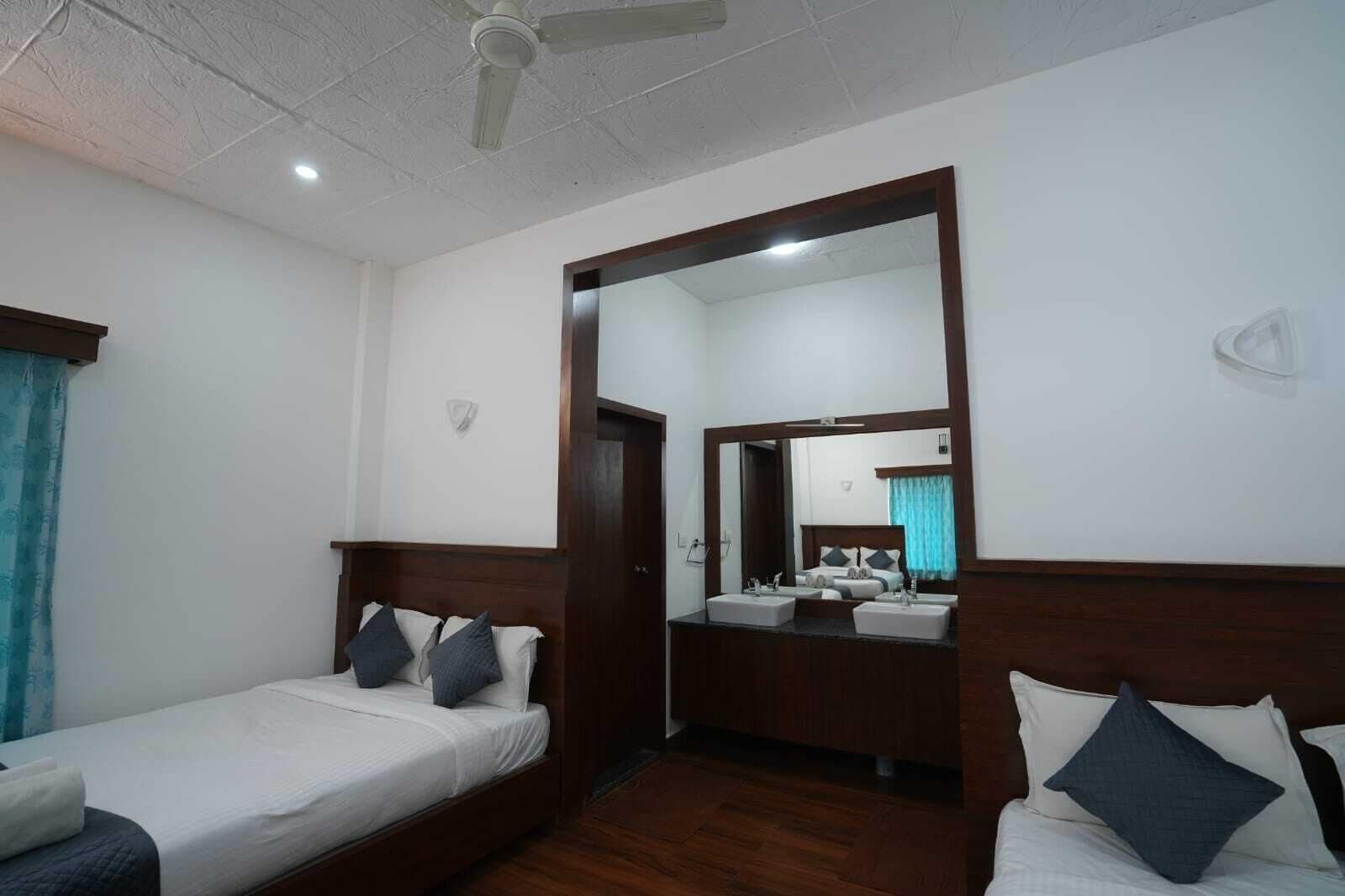 A hotel room with a single bed, a small sitting area, a bathroom with a mirror, and a ceiling fan.