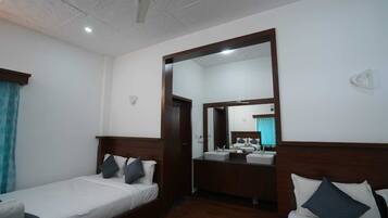 A hotel room with a single bed, a small sitting area, a bathroom with a mirror, and a ceiling fan.
