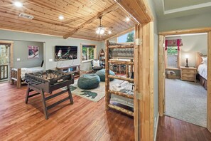 Une pièce confortable avec un baby-foot, un lit, un bureau et une fenêtre donnant sur les arbres.