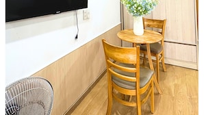 Une pièce dotée d’un téléviseur à écran plat fixé au mur, d’une table à manger en bois avec des chaises, et d’un climatiseur placé au-dessus de la table.