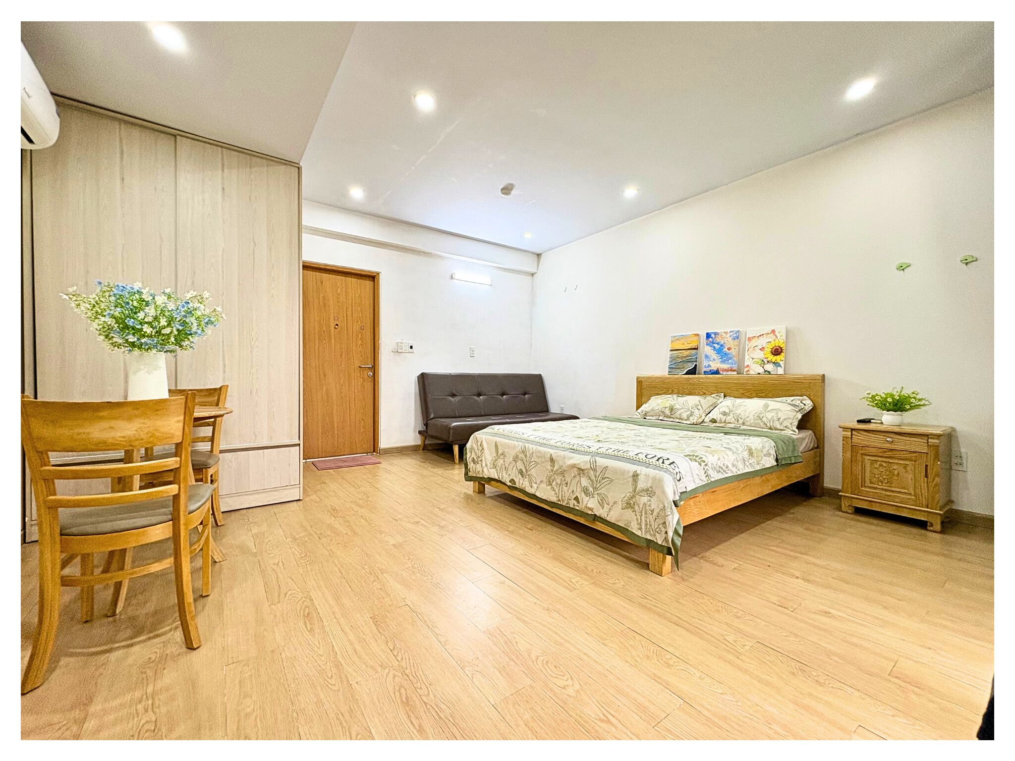 Un dormitorio con una cama, una silla de madera, una mesita con un florero y un armario.
