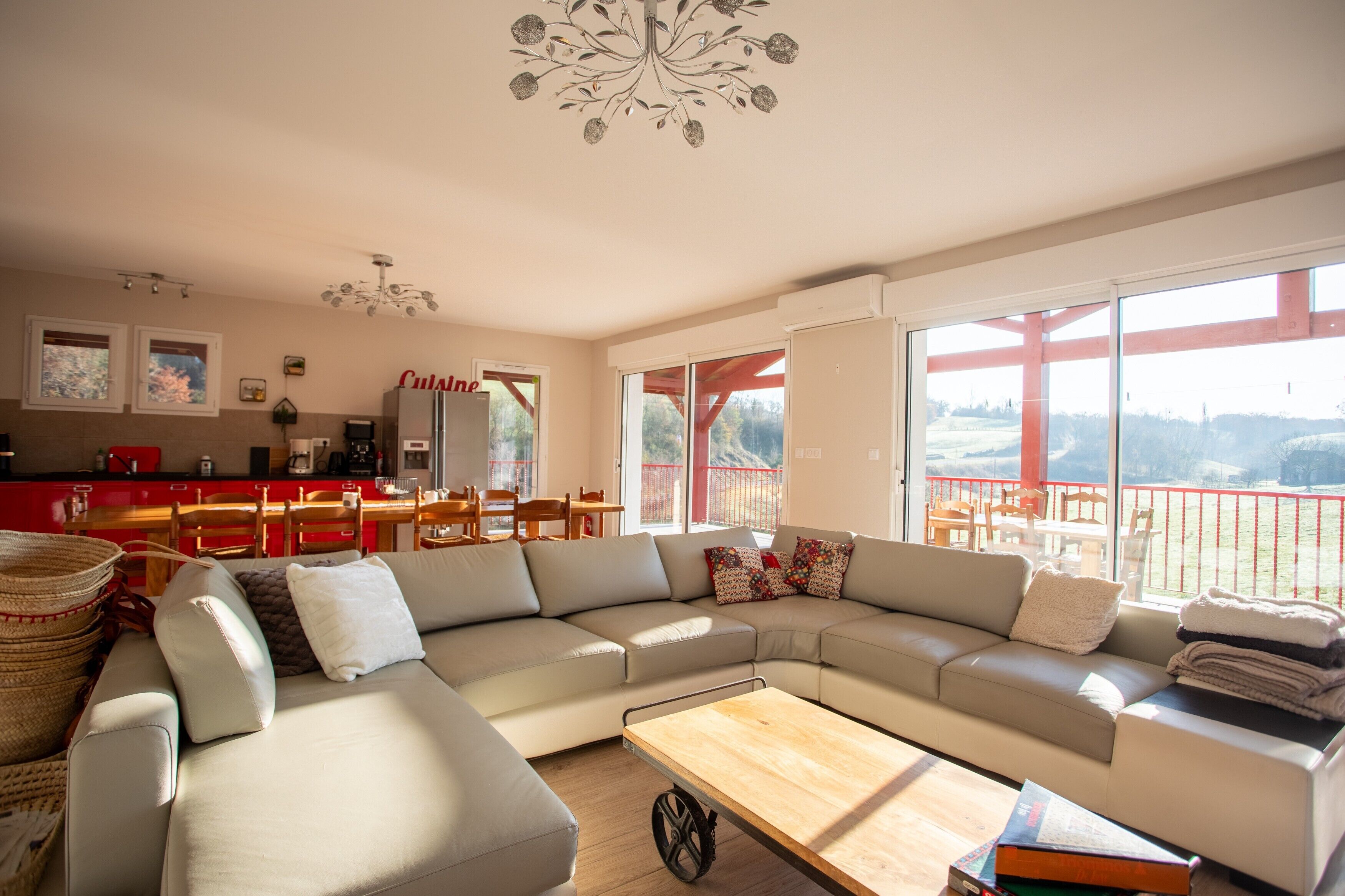 A modern living room with a large sectional sofa, a wooden coffee table, and a dining area with red chairs and a table.
