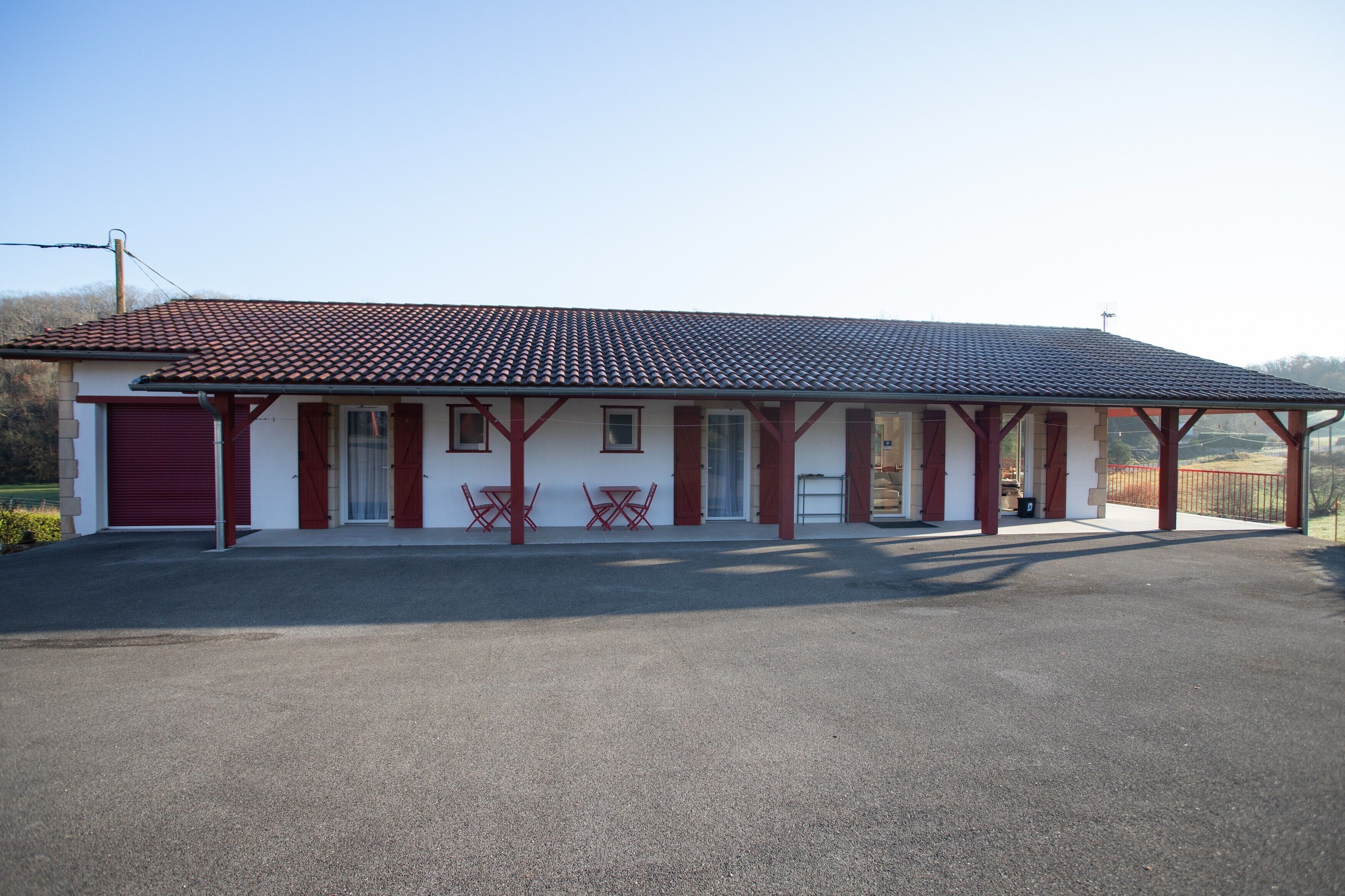 Un bâtiment d’un seul étage, avec un toit recouvert de tuiles rouges, un porche abrité et une porte de garage rouge.