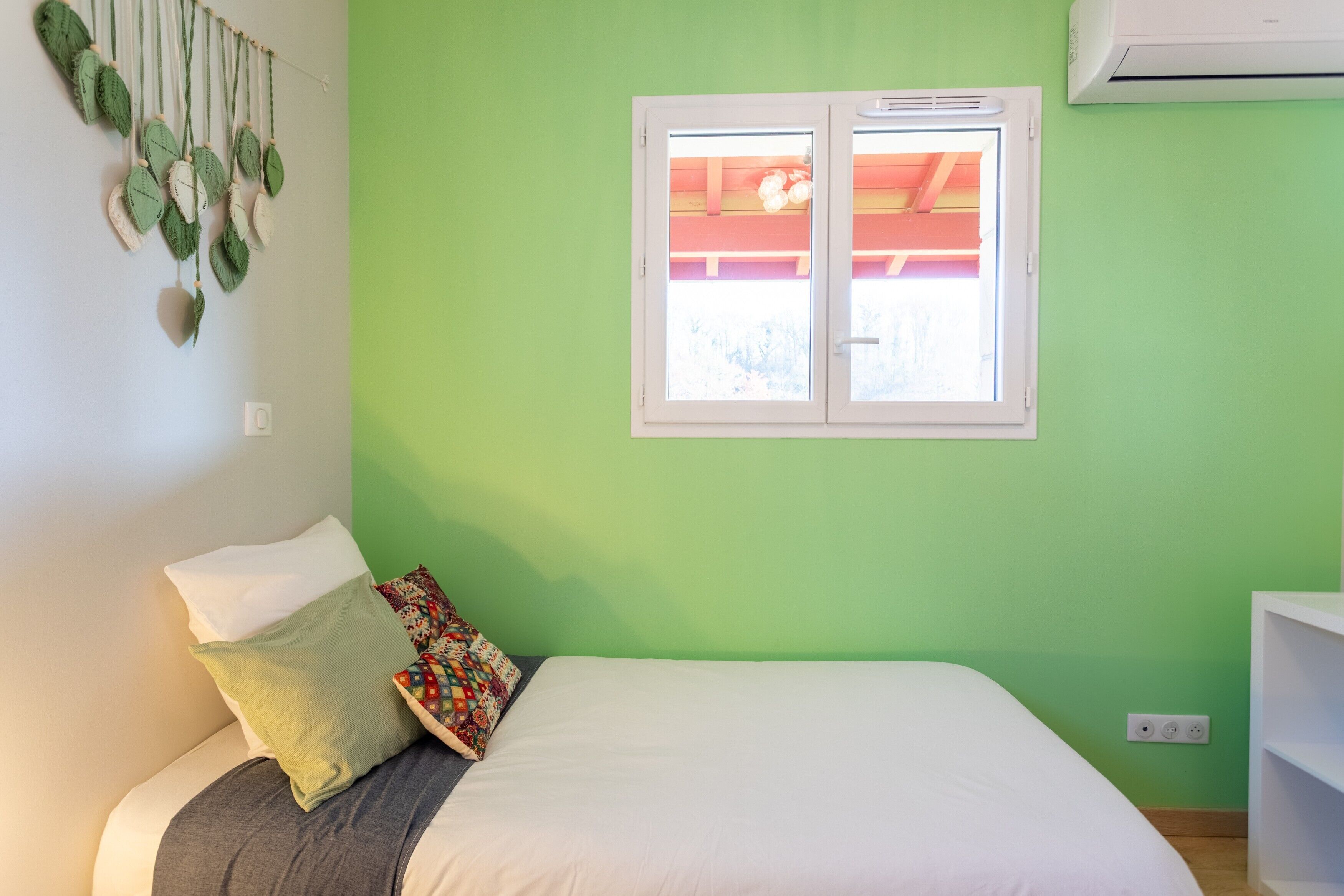 Une chambre avec un lit, des oreillers, une fenêtre et un appareil de climatisation.