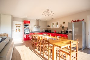 Une cuisine moderne avec des meubles rouges, un réfrigérateur en acier inoxydable et un coin repas comprenant des chaises et une table en bois.