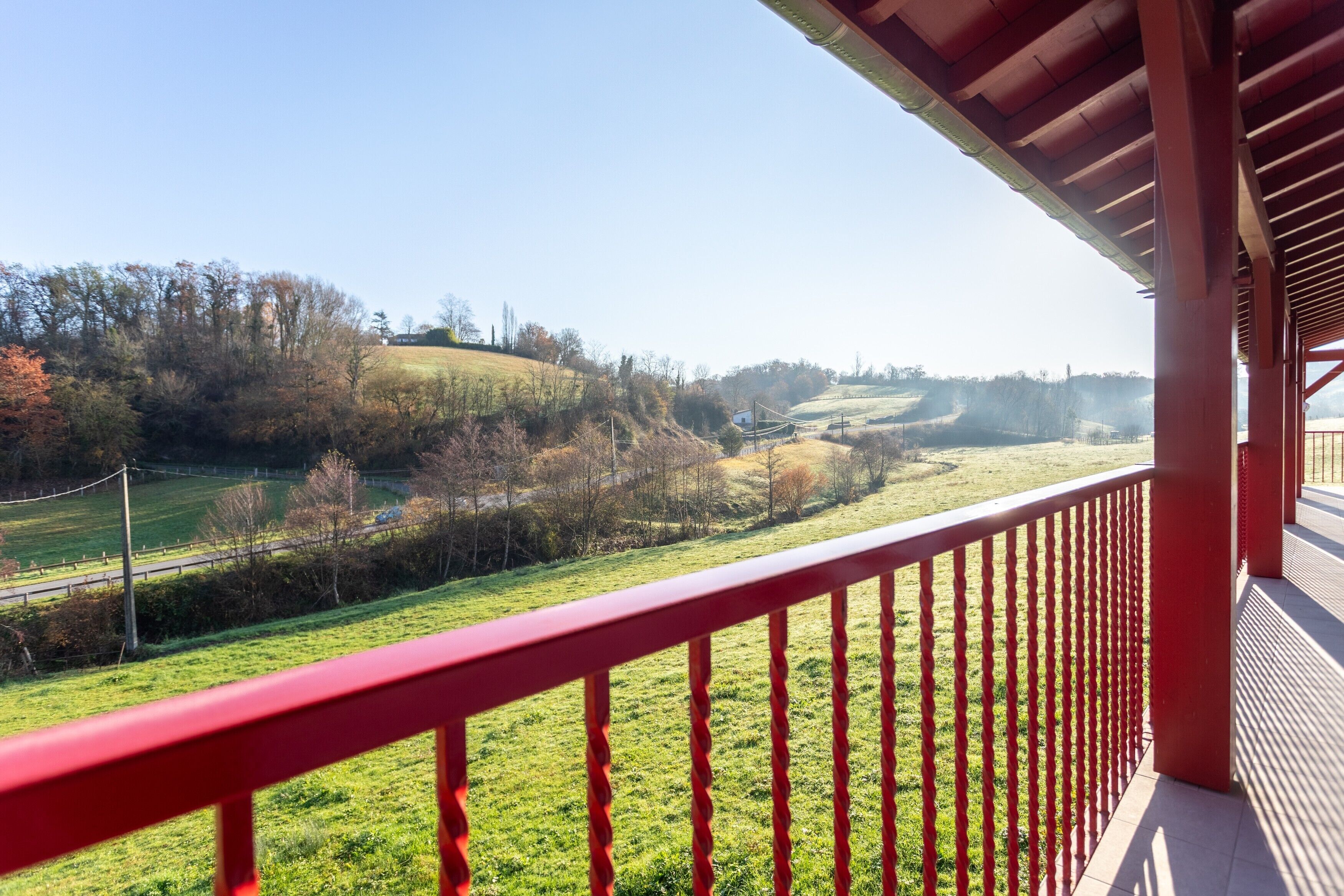 A balcony with a red railing overlooking a green landscape with hills and trees.