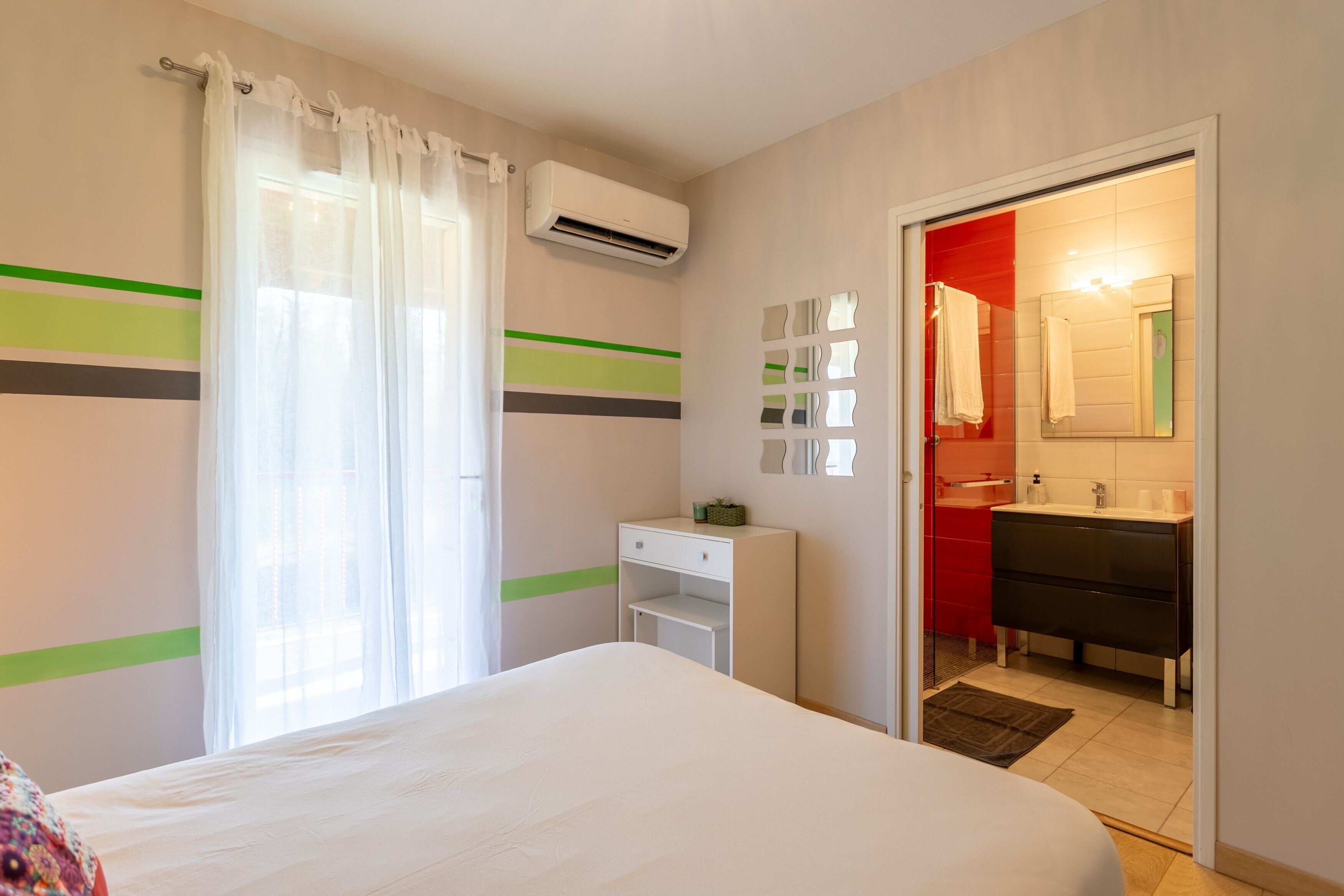 A hotel room with a bed, a desk, a mirror, and a bathroom visible through an open door.