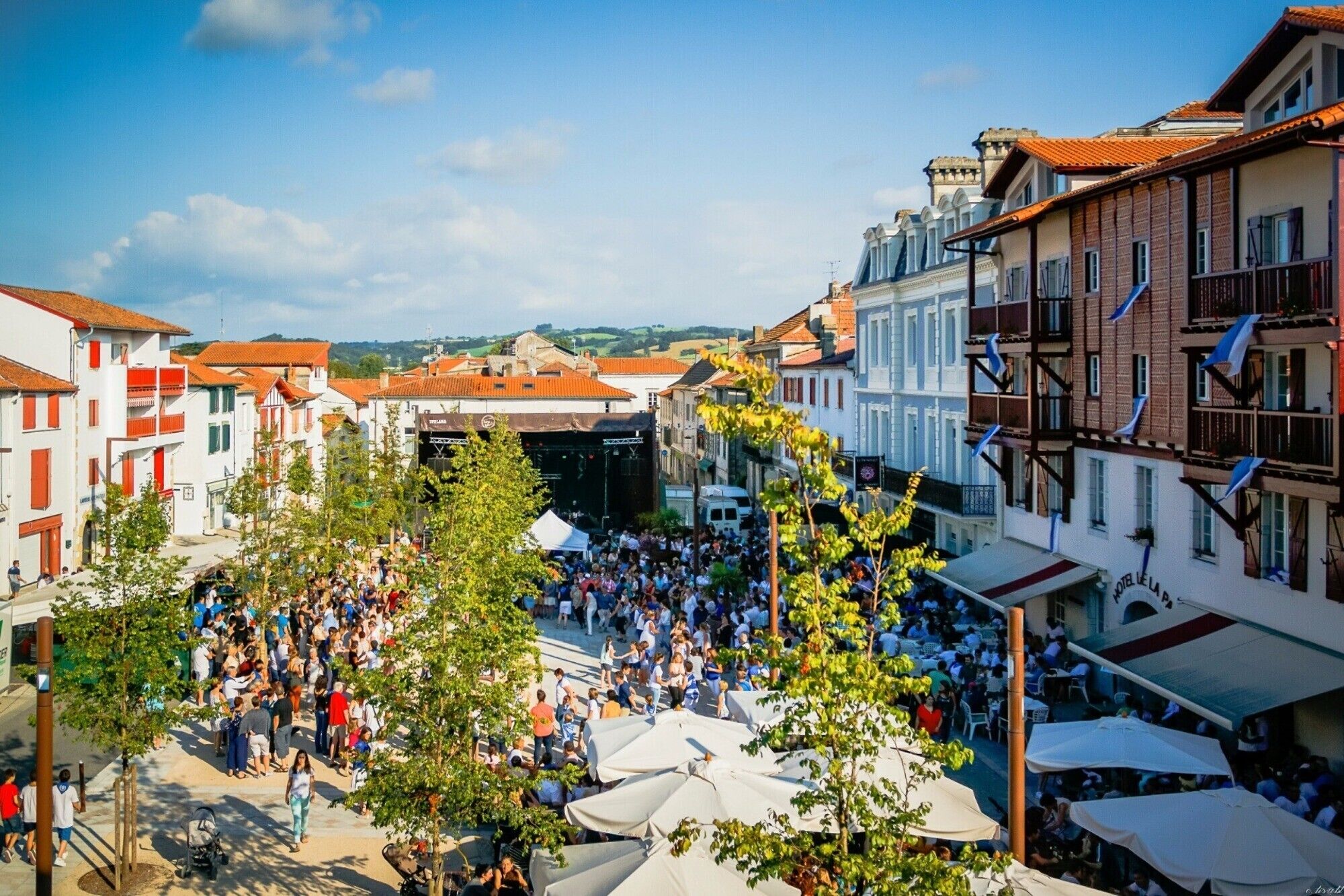 A bustling square with a crowd, surrounded by buildings with balconies and a clear sky.